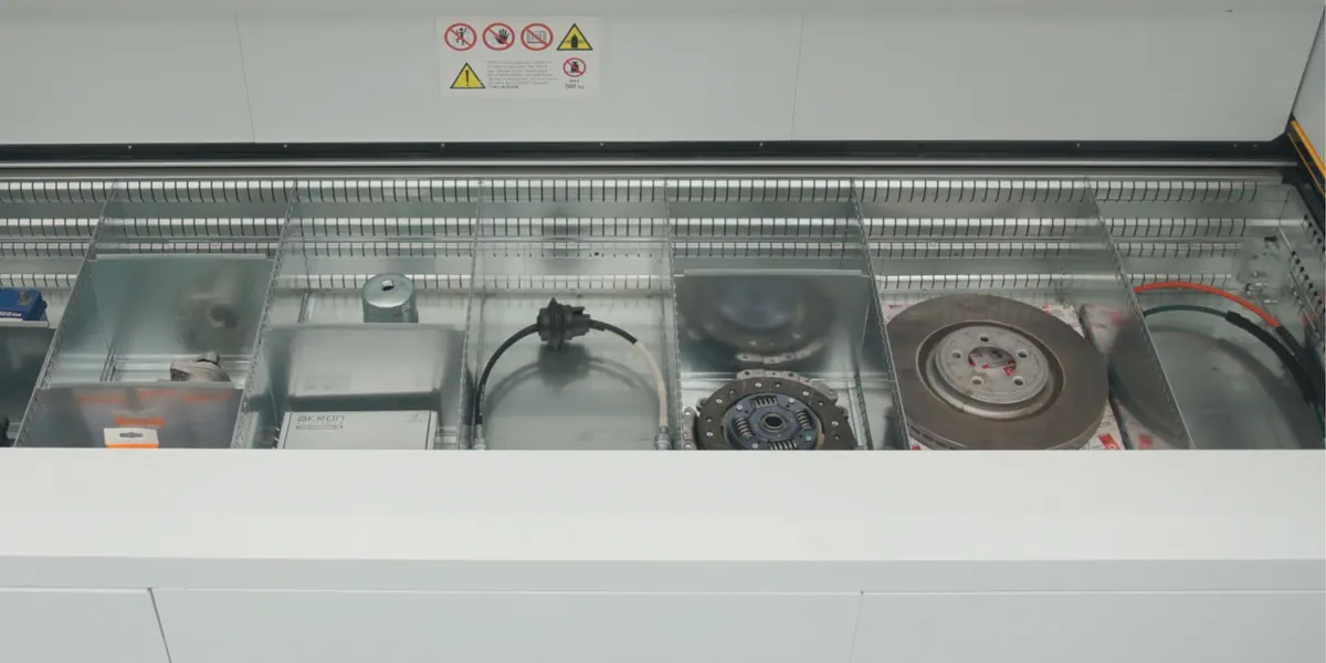 Bandeja de un almacén vertical Modula con refacciones ordenadas por compartimento: baterías, filtros, un disco de embrague y un disco de freno